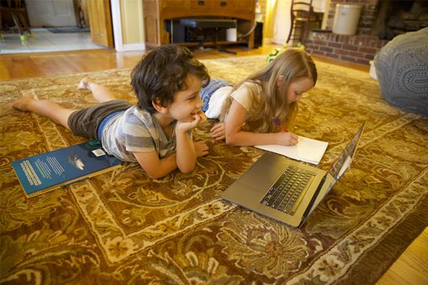 two young children laying on a rug in a living room with a laptop in front of them